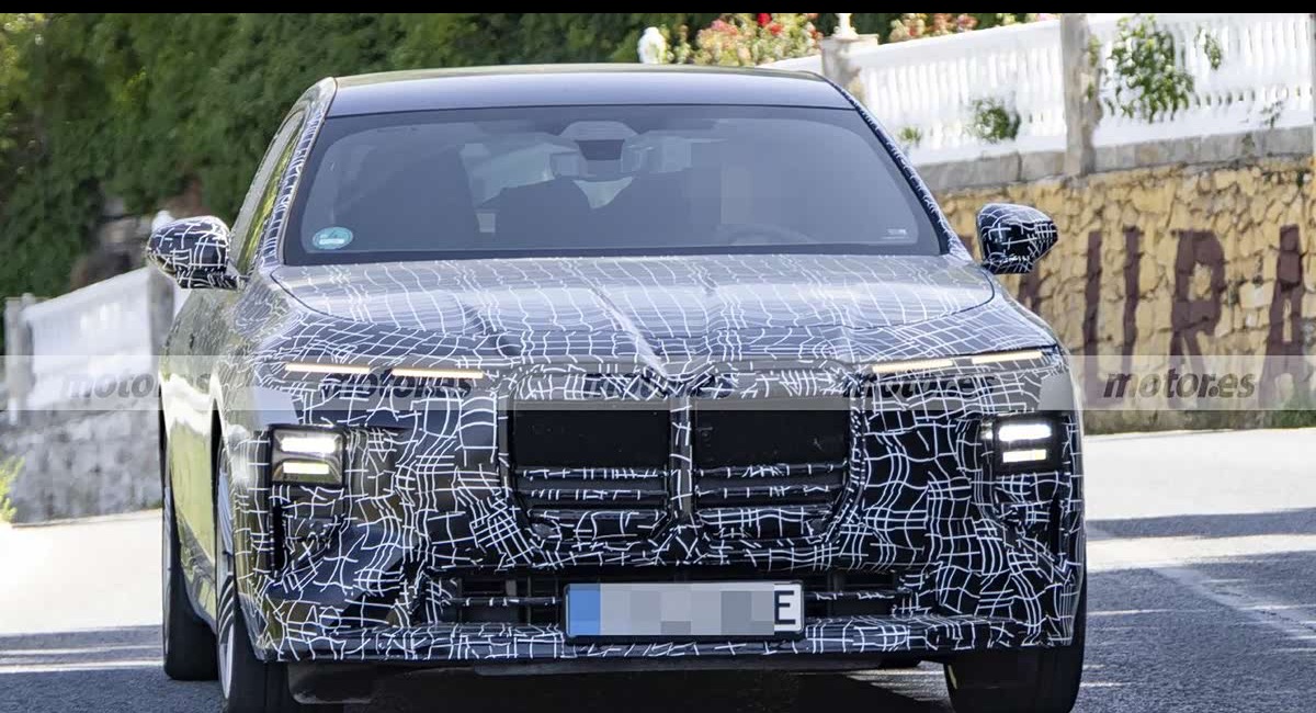 Front view of the camouflaged BMW i7 ALPINA 70 xDrive prototype with amber daytime running lights