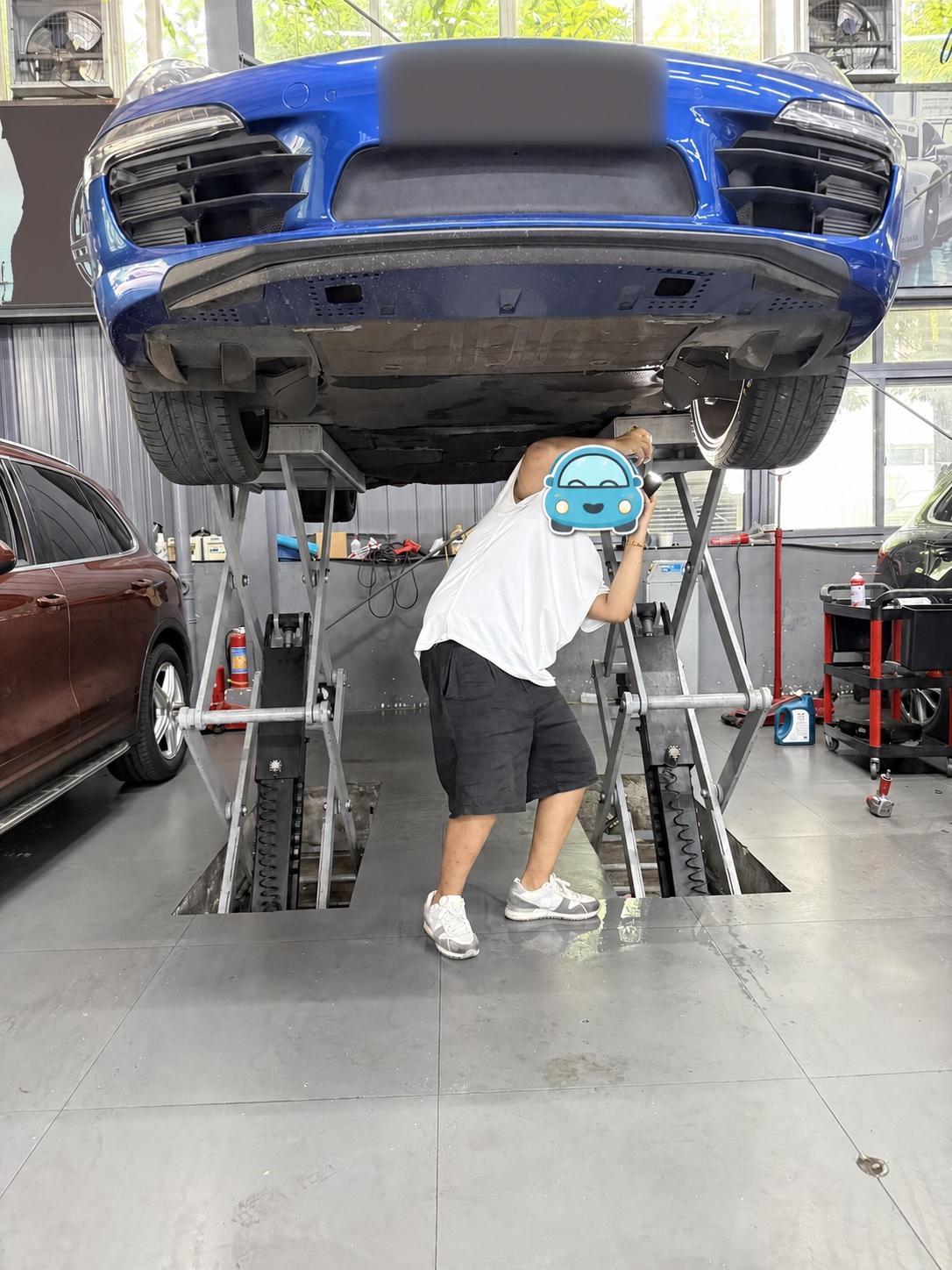 Blue 2015 Porsche 911 Carrera raised on a workshop lift for underbody inspection