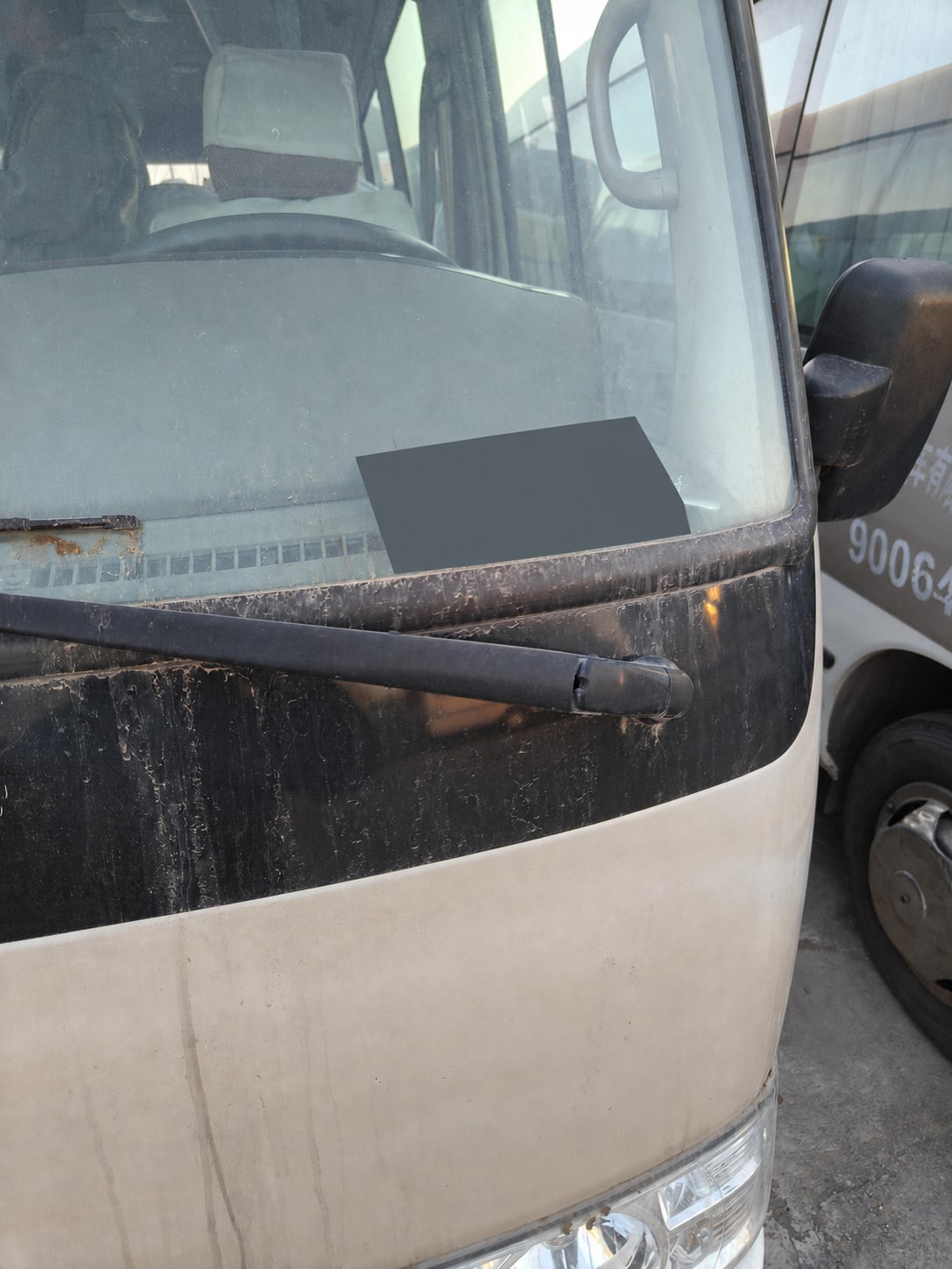Front windshield and exterior condition of a used Coaster-style bus with its registration plate redacted