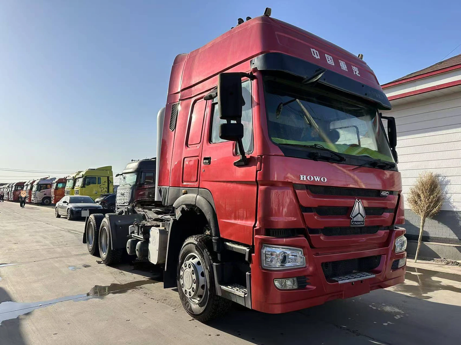 Supplier-provided front three-quarter view of a red HOWO tractor truck in a vehicle yard