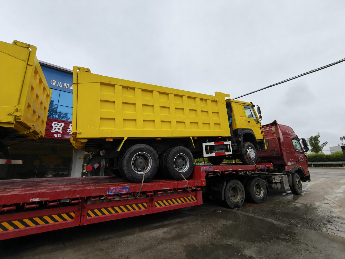 Yellow HOWO dump truck transported from the supplier facility on a flatbed trailer
