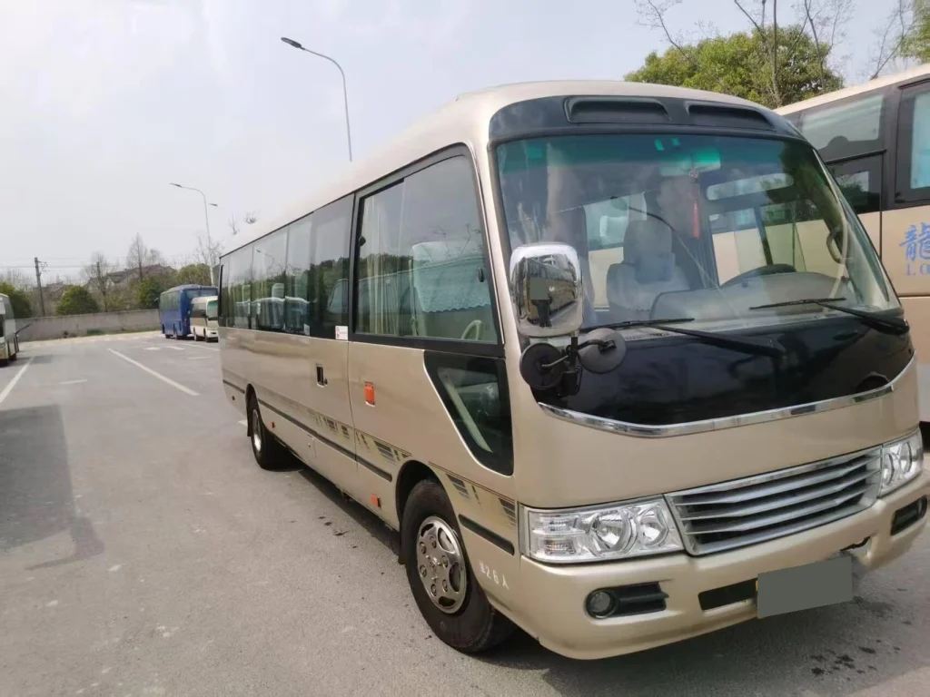 Beige used Coaster-style bus viewed from the front side during sourcing for the Ghana project